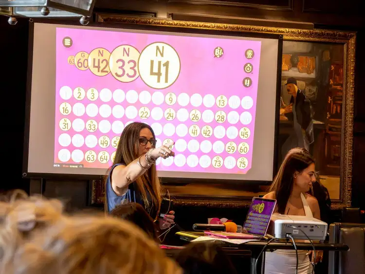 Maggie Sitar calling numbers at Lucky Ladies Social & Bingo, the bingo board glowing pink behind her